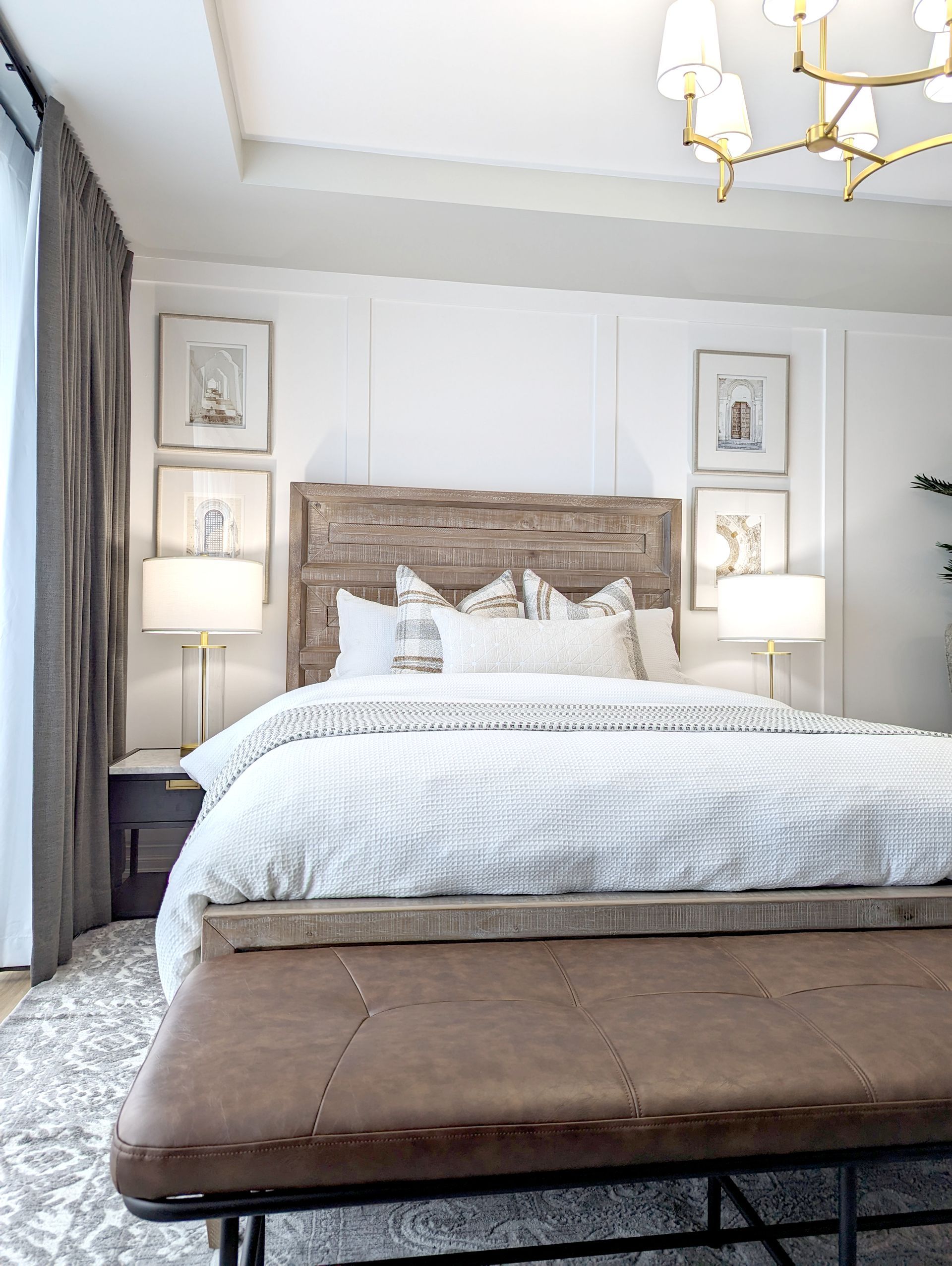 Cozy bedroom with a rustic wooden headboard, framed art, and a leather bench. Neutral tones and soft lighting.