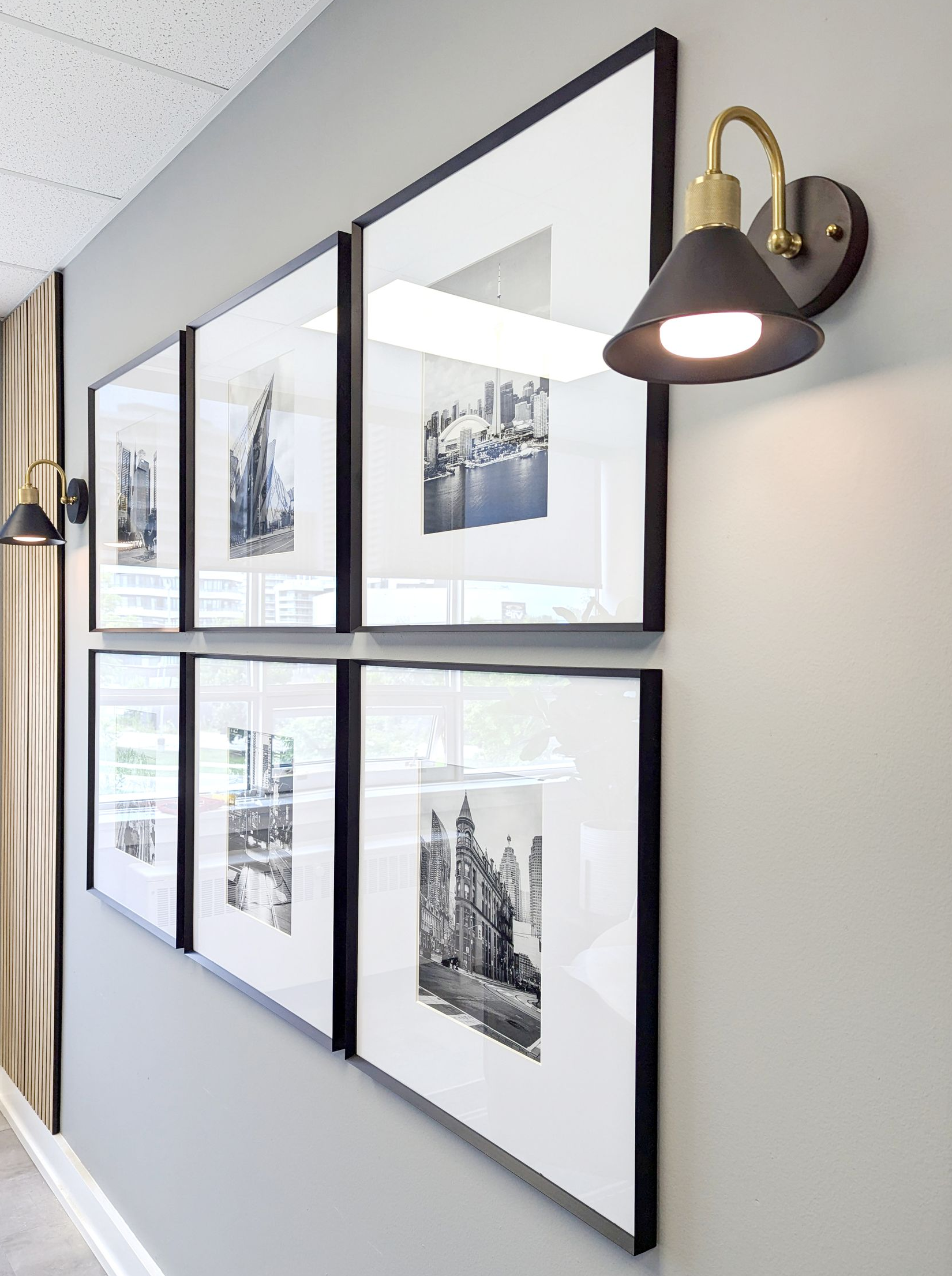 Wall with framed black and white photos, sconce lighting. Gray wall, black frames, white mats.