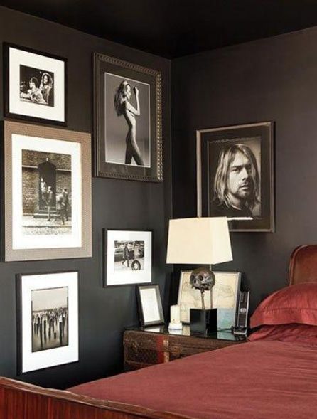 Black and white framed photographs on a dark wall in a bedroom, above a bedside table with a lamp and red bedding.
