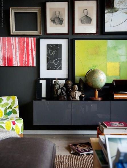 Dark wall with a gallery of framed art, a floating cabinet holding sculptures and a globe, and a patterned chair.