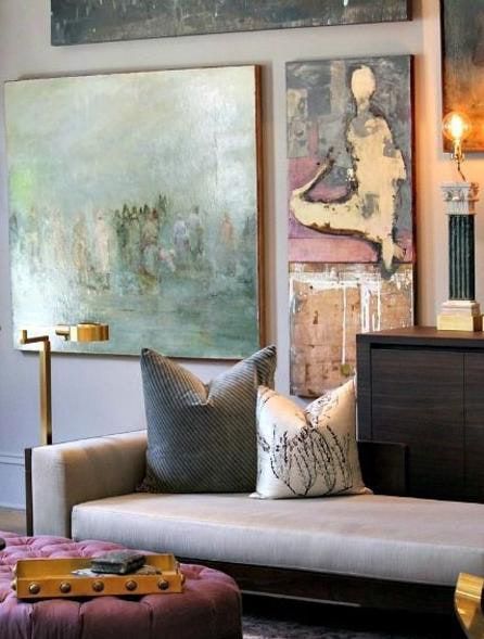 Couch with decorative pillows, artwork on the wall, and a purple ottoman. Muted colors and modern design.