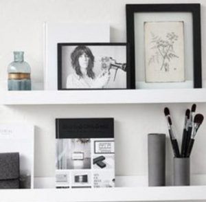 Shelves with framed photos, decorative items, and makeup brushes in a bright room.
