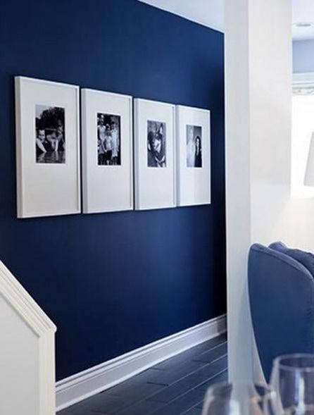 Four framed black and white photos on a navy blue wall, white trim, and part of a sofa.
