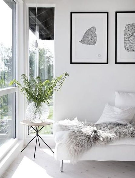 White minimalist living room with plants, artwork, and fur throw.