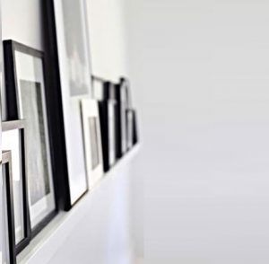 Black-framed photos on a white shelf against a white wall, in varying sizes, arranged horizontally.
