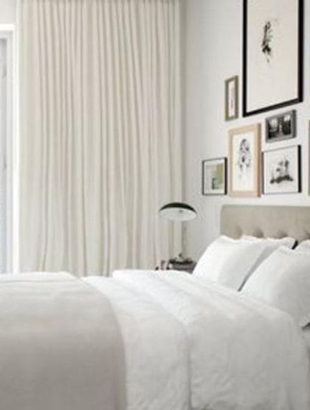 White bedroom with bed, curtains, art gallery wall, and lamp.