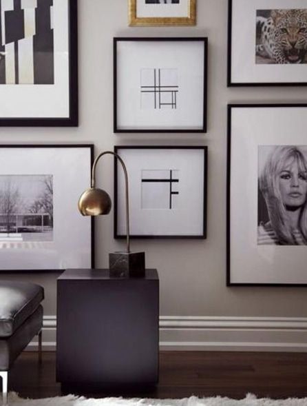 Gallery wall with black and white framed art, a modern lamp, and a dark side table.