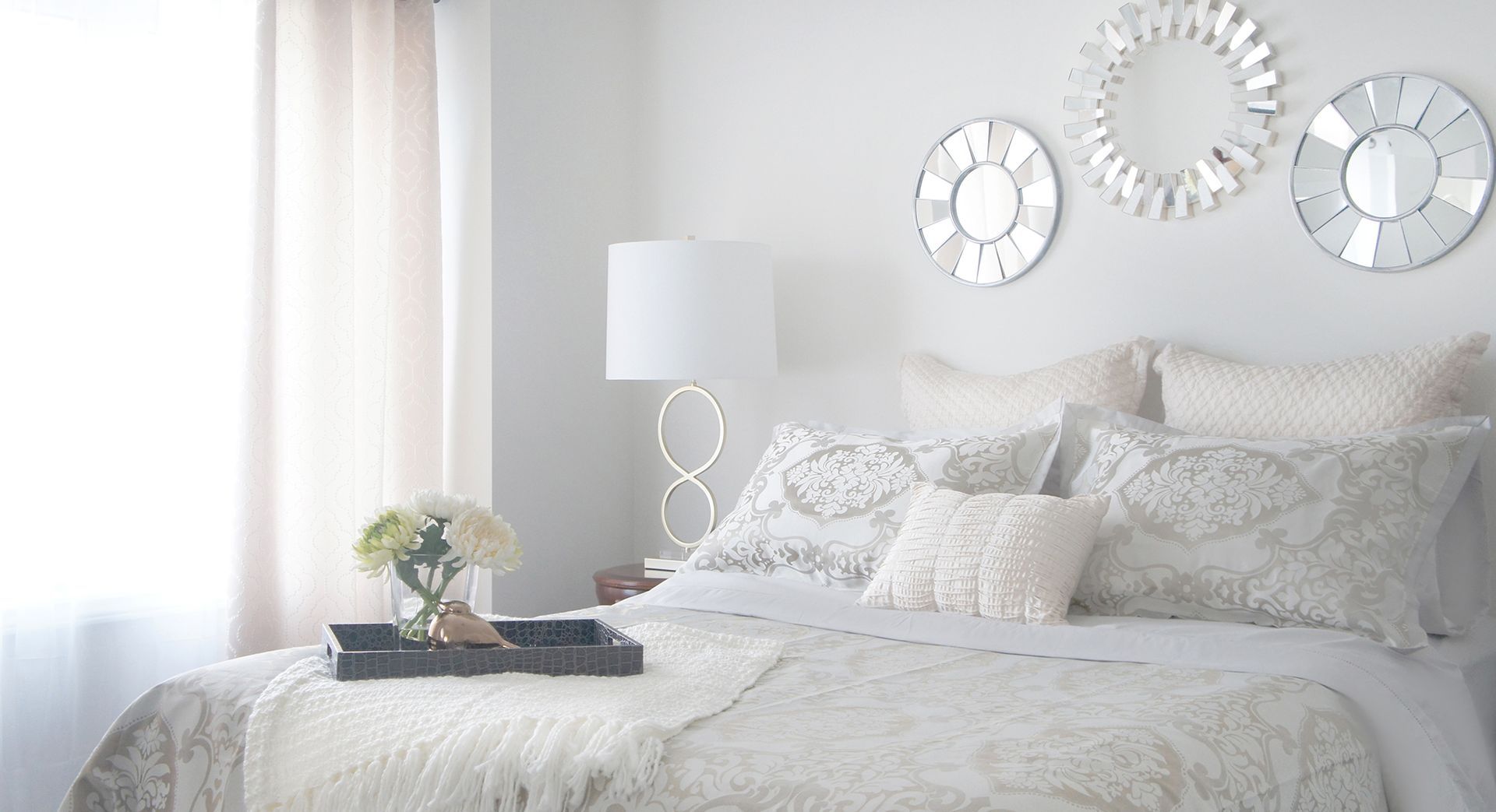 Bedroom with white bed, decorative pillows, and mirrored wall art.