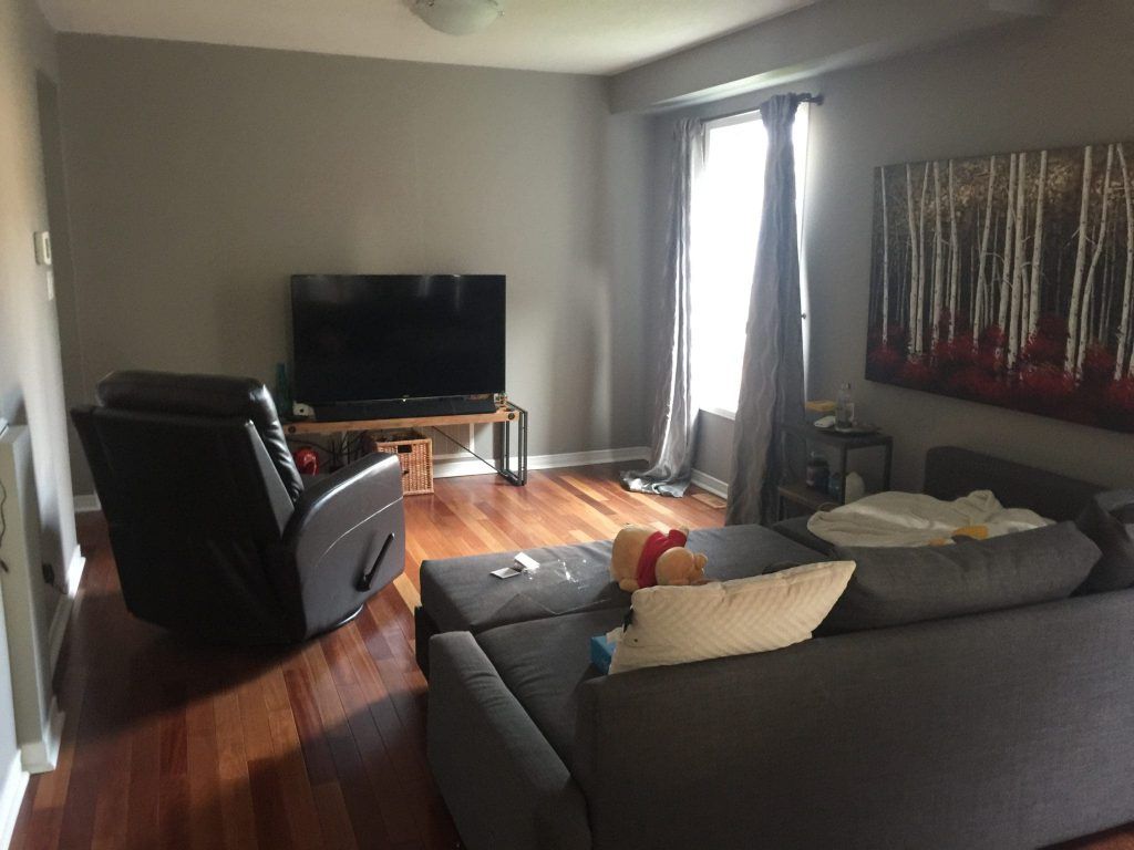 Living room with a TV, recliner, sectional sofa, and artwork. Gray walls and hardwood floors.