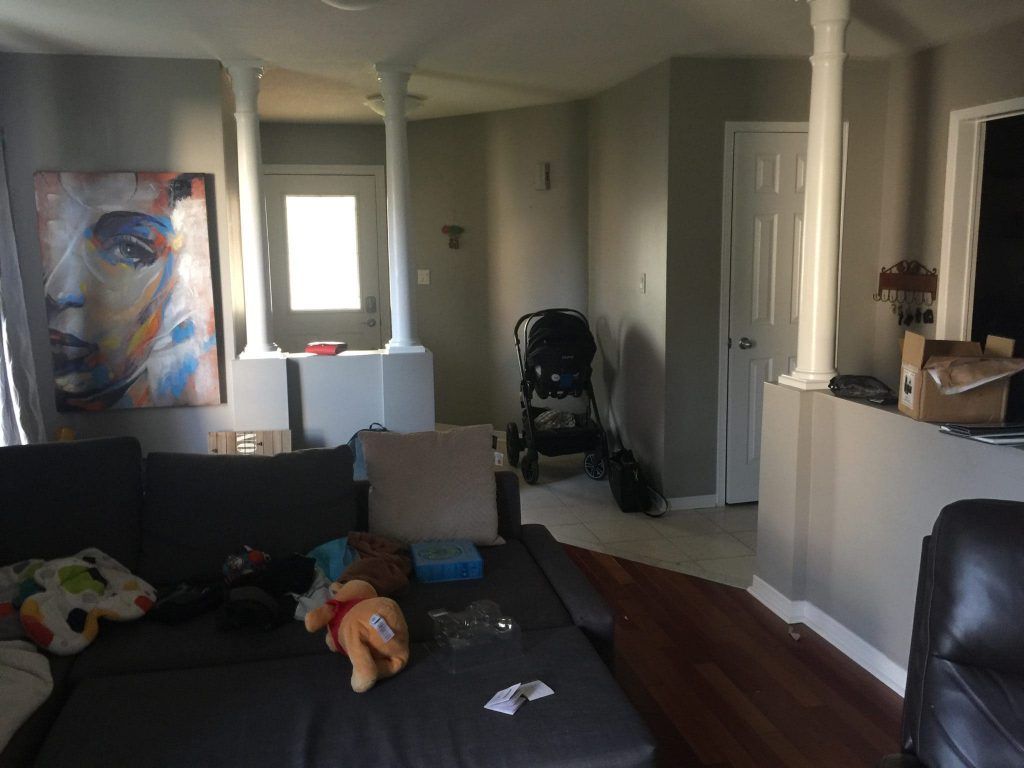 Living room with grey sectional sofa, artwork, baby stroller, door and columns.