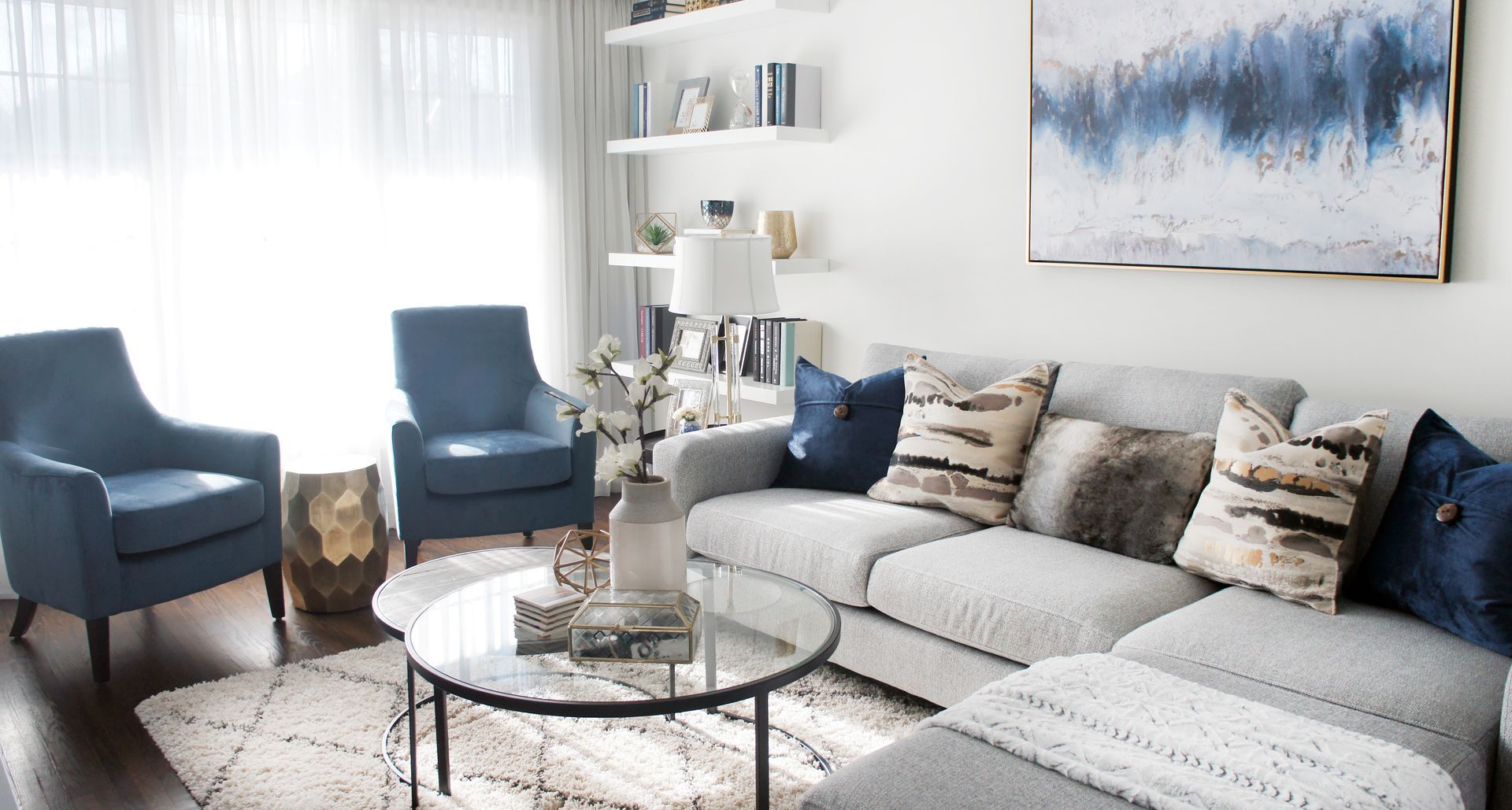 Living room with blue armchairs, gray sectional sofa, and white walls, decorated in blue and neutral tones.