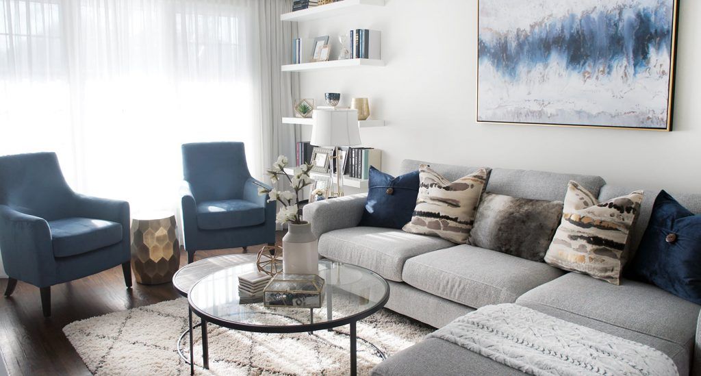 Living room with blue armchairs, grey sectional, and abstract blue painting.