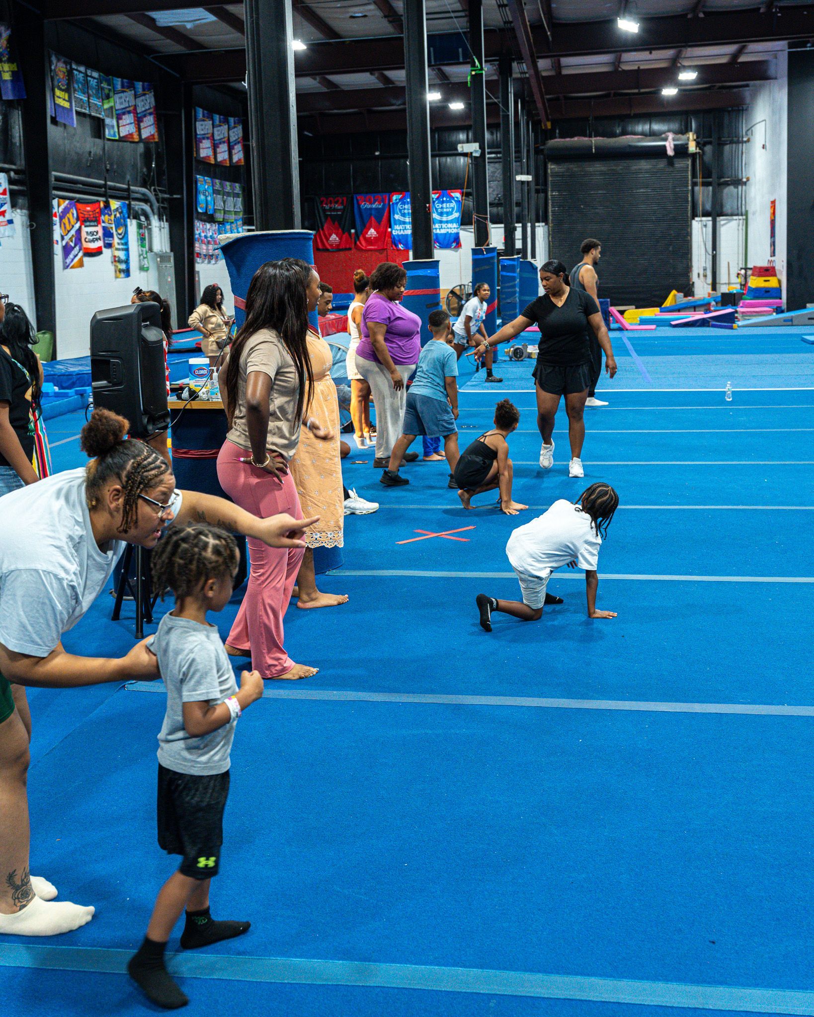 Children in a gymnastics gym doing activities on blue mats, supervised by adults.