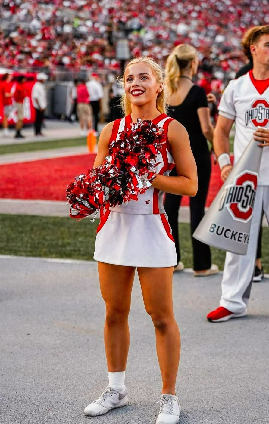 A cheerleader is holding pom poms on a football field.
