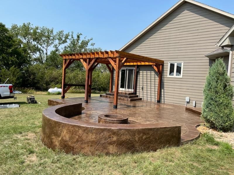 A patio with a pergola and a fire pit in front of a house.