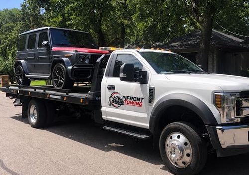 White tow truck hauling a black SUV on a flatbed trailer outdoors by trees