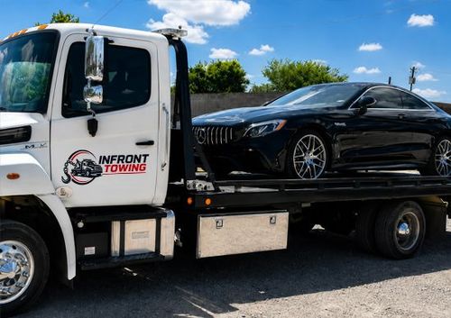 Tow truck carrying a black sports car on a flatbed under a blue sky