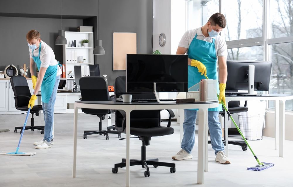 Two people wearing masks and aprons mopping an office floor.