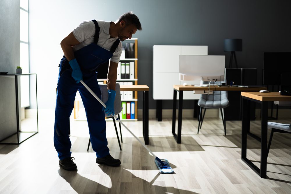 Man in blue cleaning suit mopping office floor with blue mop.