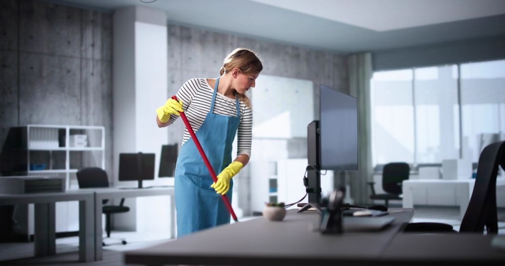 Woman in gloves and apron cleaning office floor with a mop.