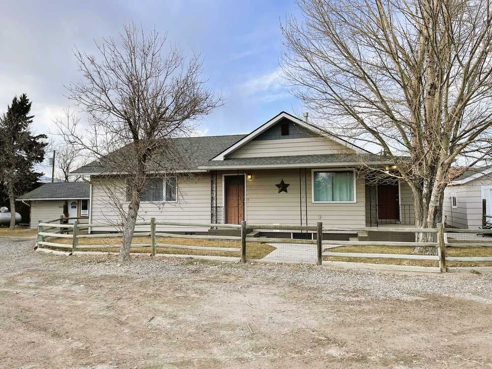 A light tan one-story house with a wooden fence in front, bare trees and a cloudy sky.