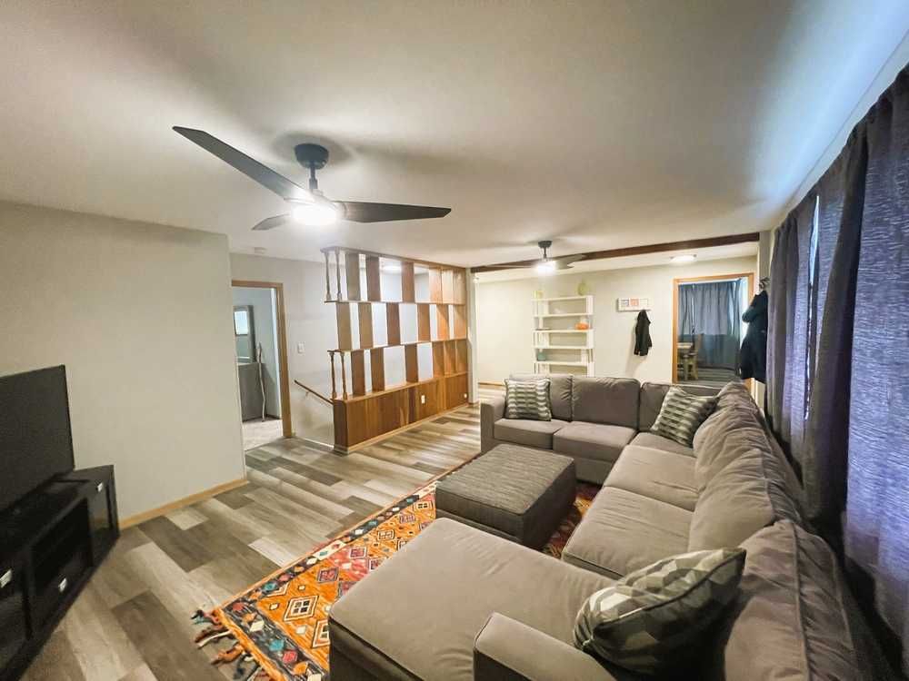 Spacious living room with sectional sofa, rug, and decorative wall divider. Gray walls and flooring.