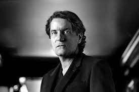 Een zwart-witfoto van een man in een pak die in een kamer staat.