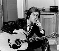 Een man zit op de grond en houdt een akoestische gitaar vast.