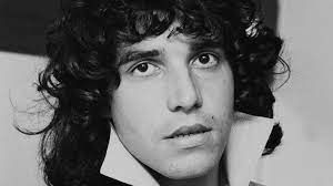 Een zwart-witfoto van een man met krullend haar en een witte kraag.