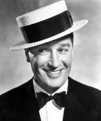 Een man met een hoed en vlinderdas glimlacht op een zwart-witfoto.