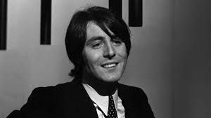 Een man in pak en stropdas lacht op een zwart-witfoto.