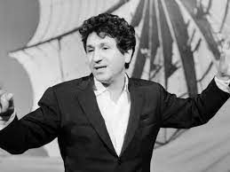 Een man in pak staat op een podium met zijn armen uitgestrekt.