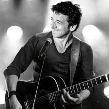 Een man speelt gitaar en zingt in een microfoon op een podium.