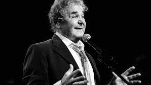 Een man in pak en stropdas zingt in een microfoon.