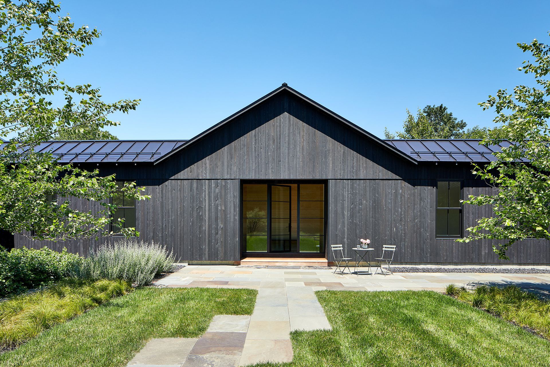The front of a black house with a roof and a walkway leading to it.