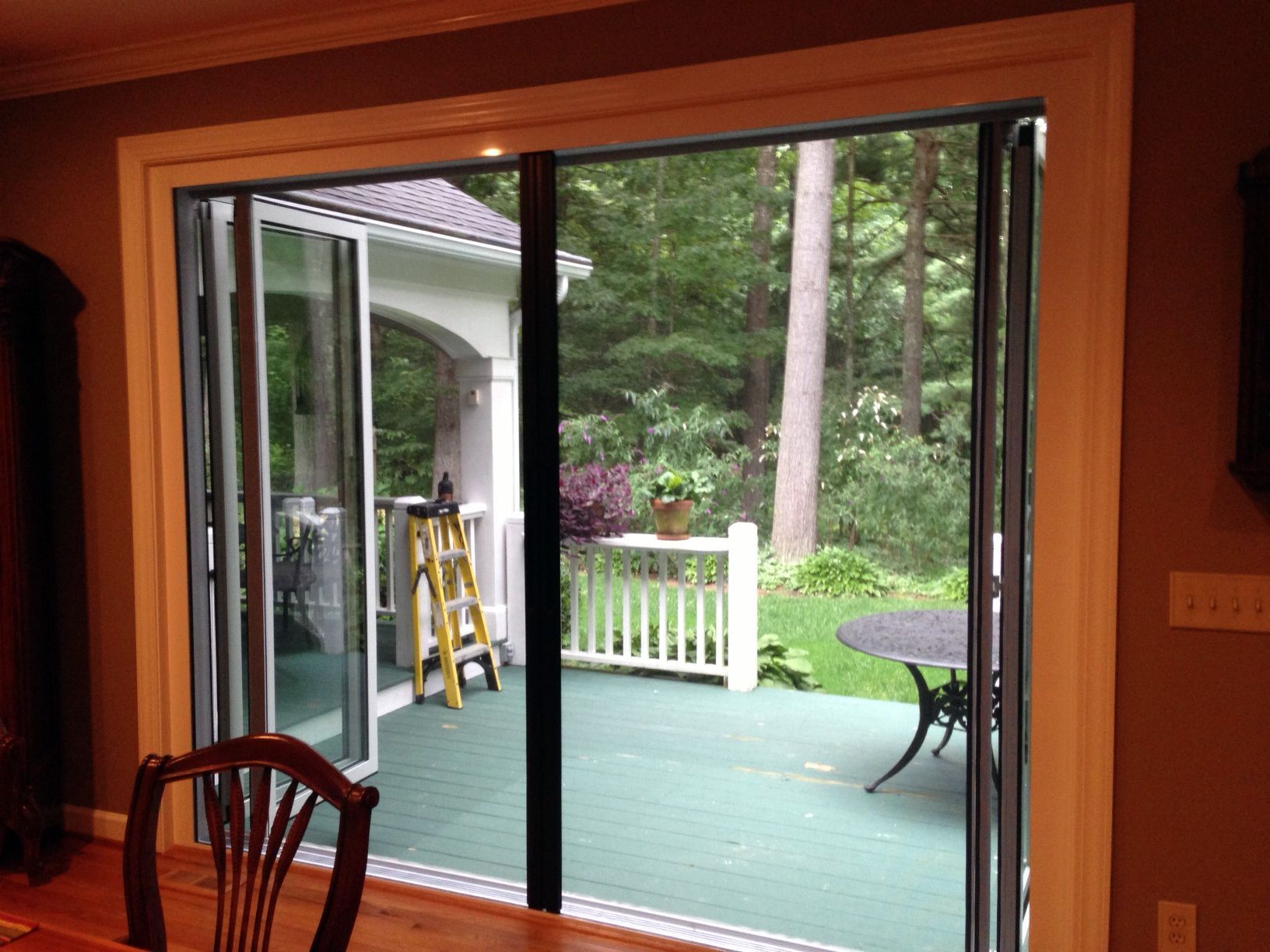 A sliding glass door is open to a deck with a table and chairs.
