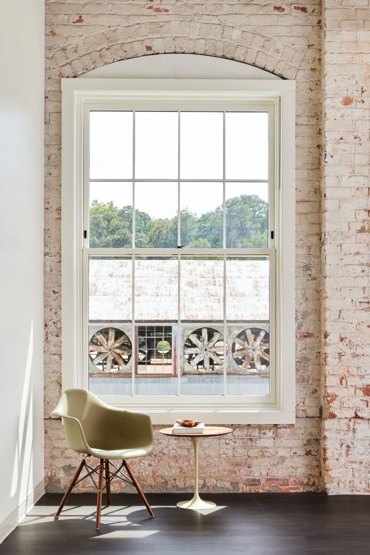 A chair is sitting in front of a large window in a room with a brick wall.