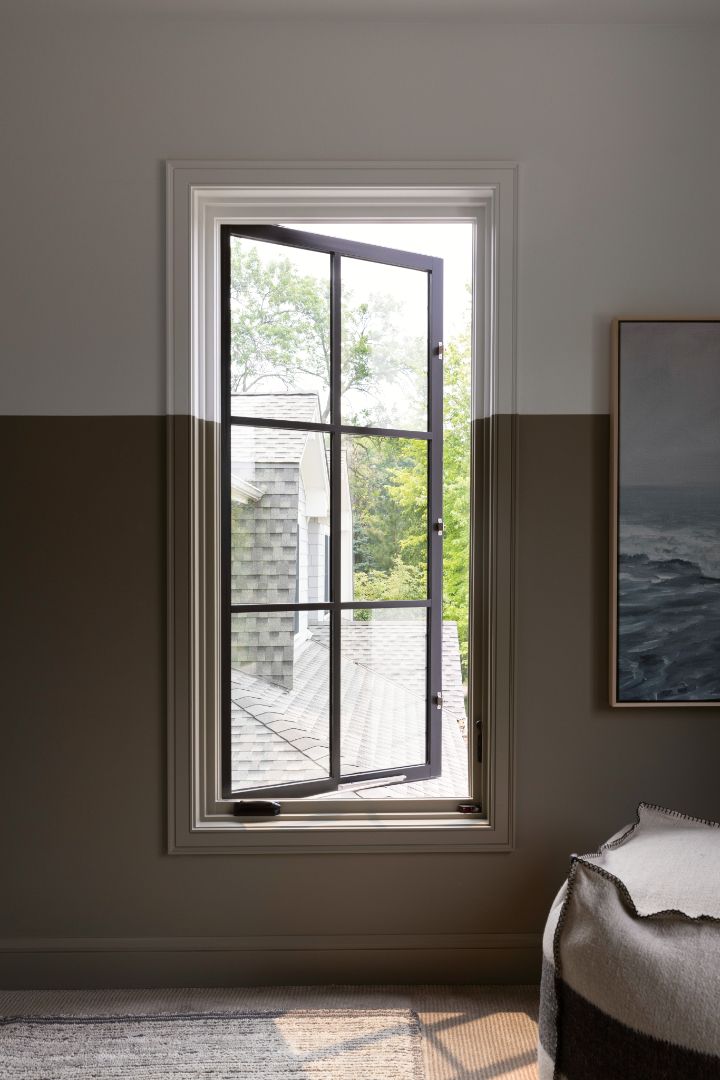 A bedroom with a large window and a painting on the wall.