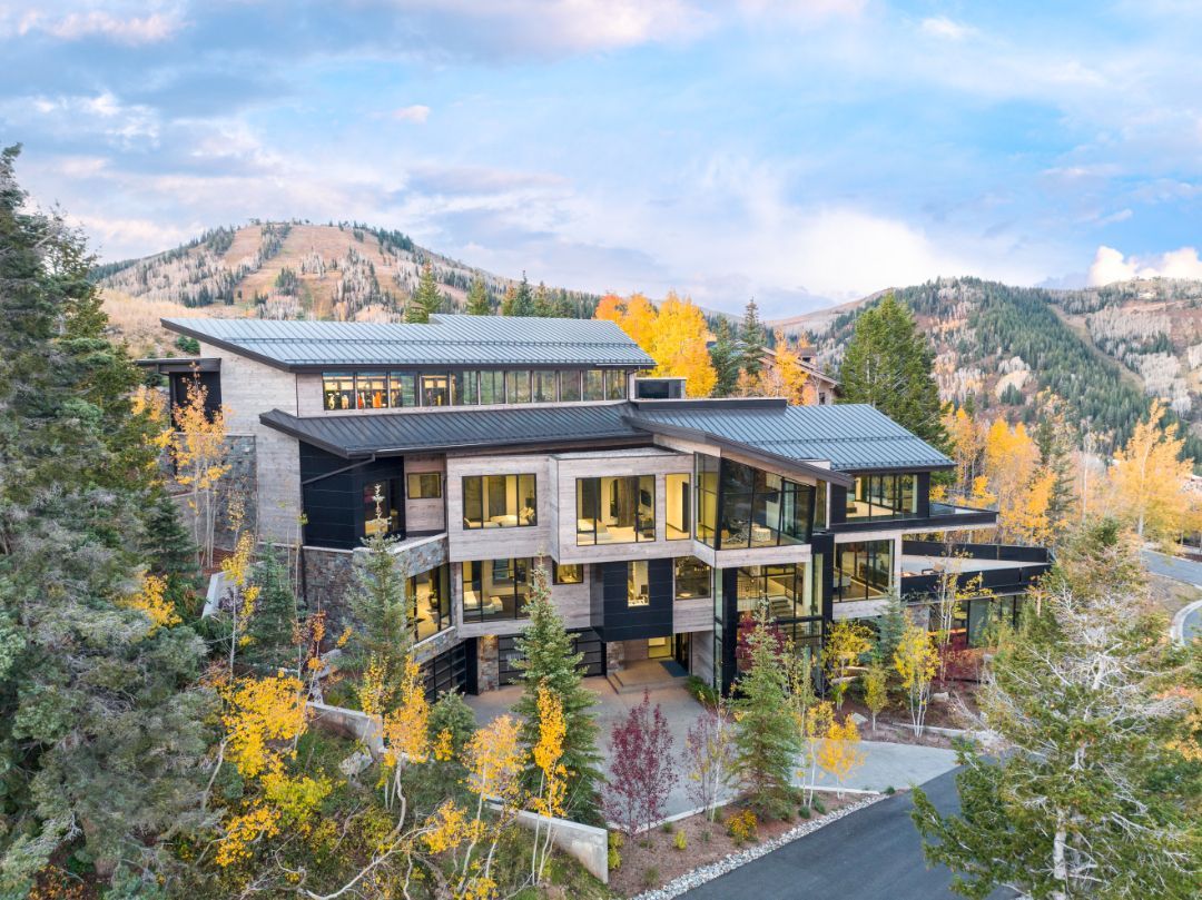 An aerial view of a large modern house surrounded by trees and mountains.