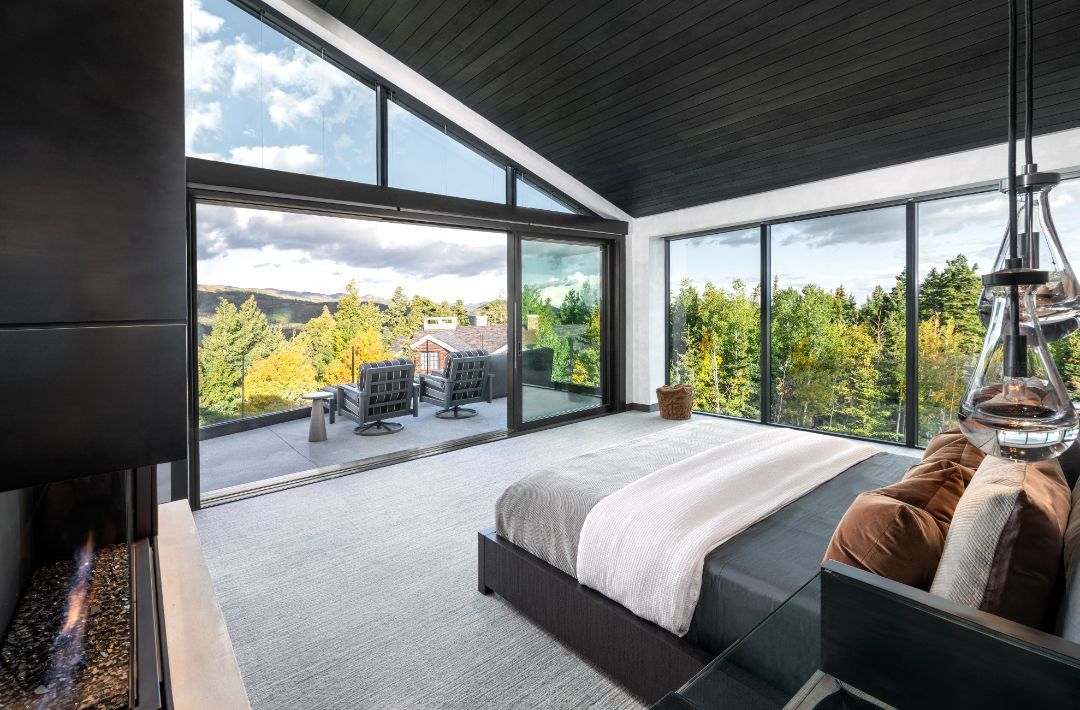 A bedroom with a large bed , fireplace and lots of windows.