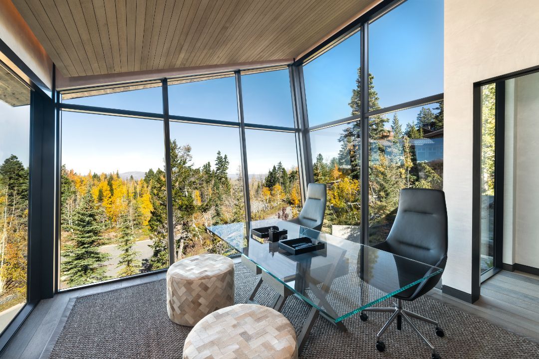 There is a desk and chair in the room with a lot of windows.