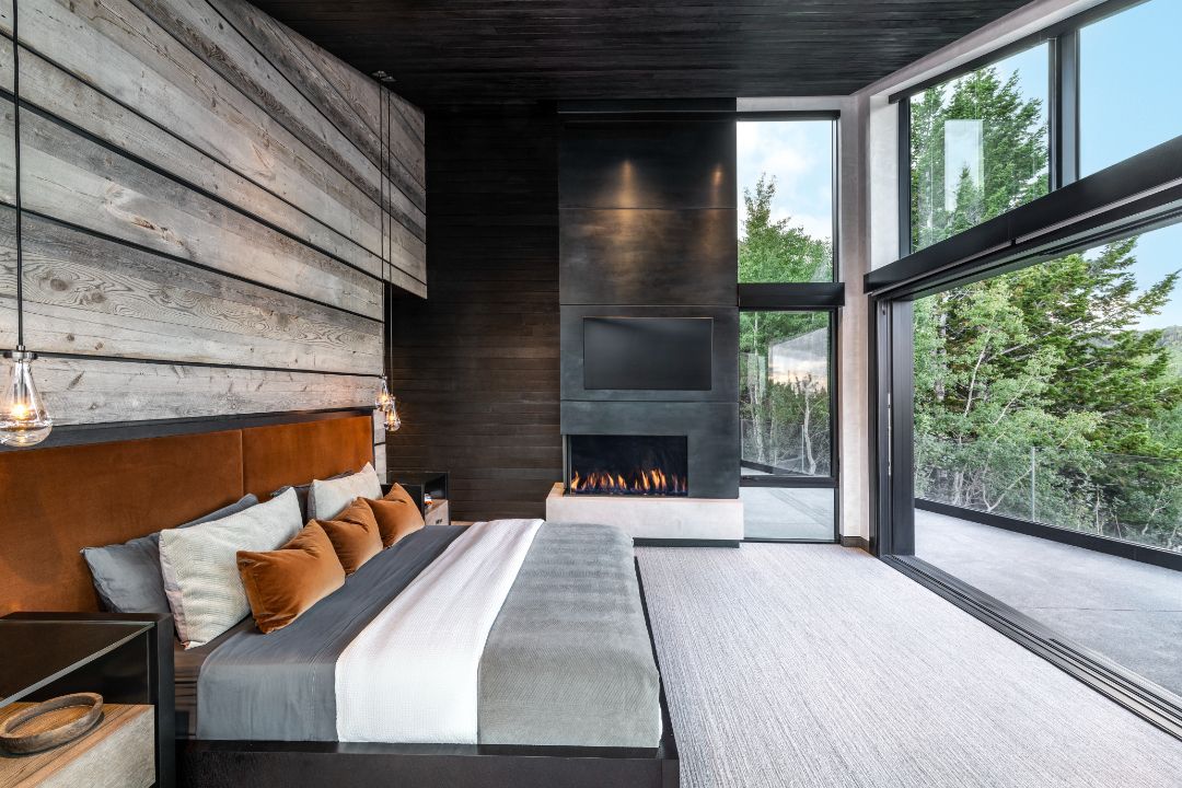 A bedroom with a large bed , fireplace , television and large windows.