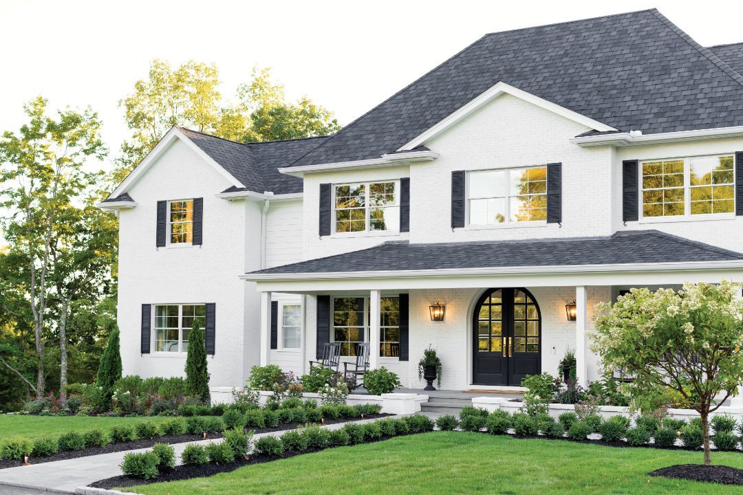 A large white house with black shutters and a lush green lawn.