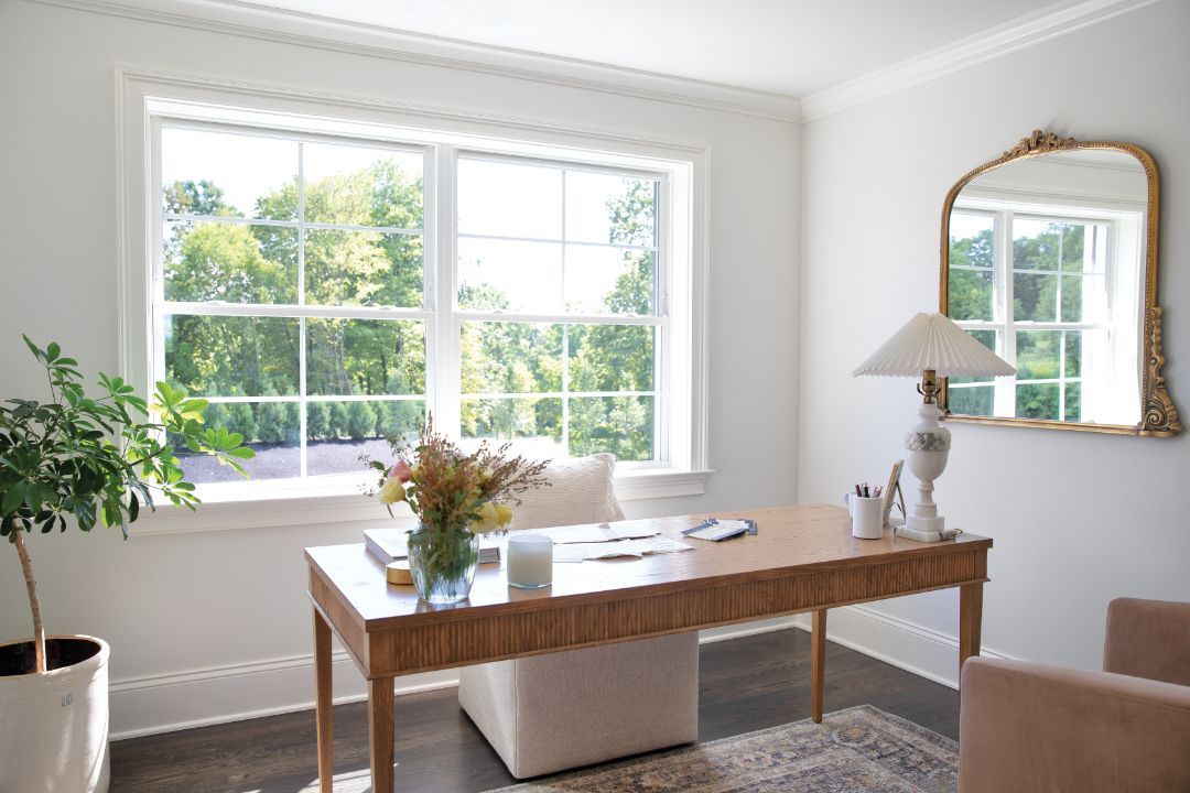 A home office with a desk , chair , lamp and mirror.