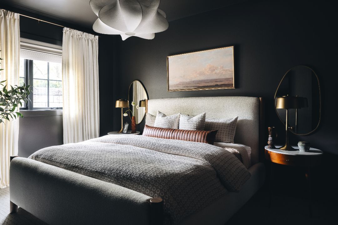 A bedroom with a bed , nightstand , mirror and painting on the wall.