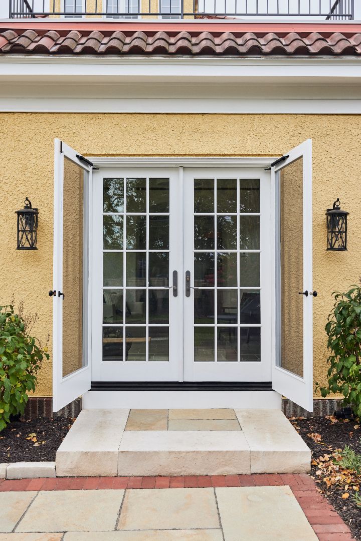 A pair of white french doors are open on a yellow house.