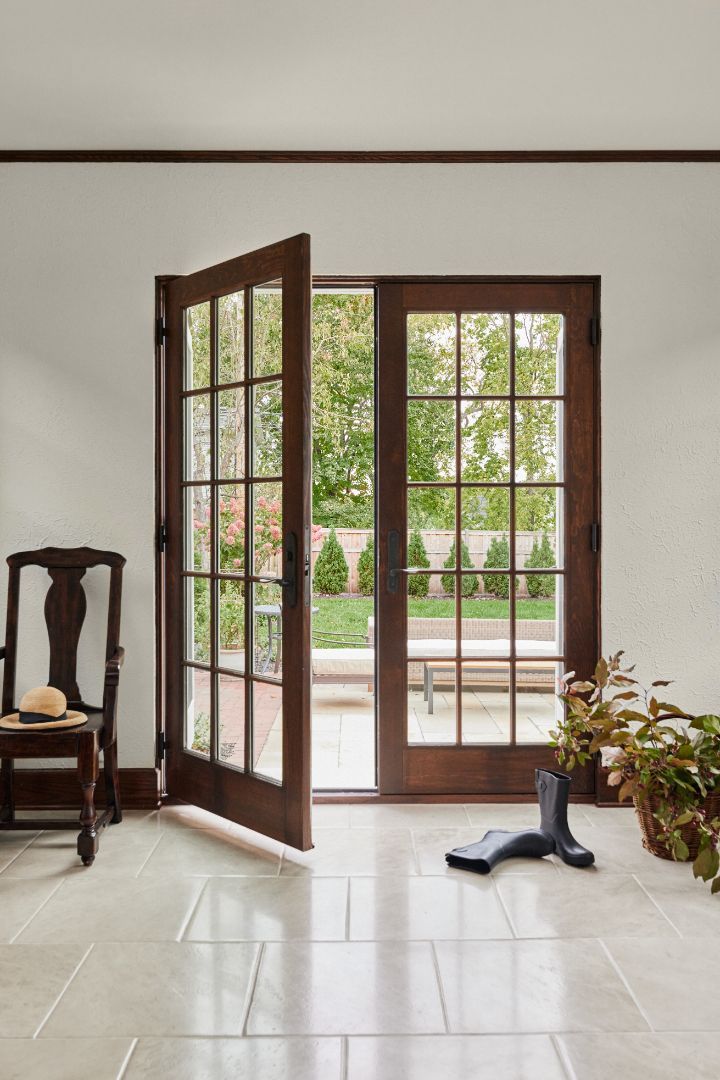 A living room with a chair , table and french doors open.