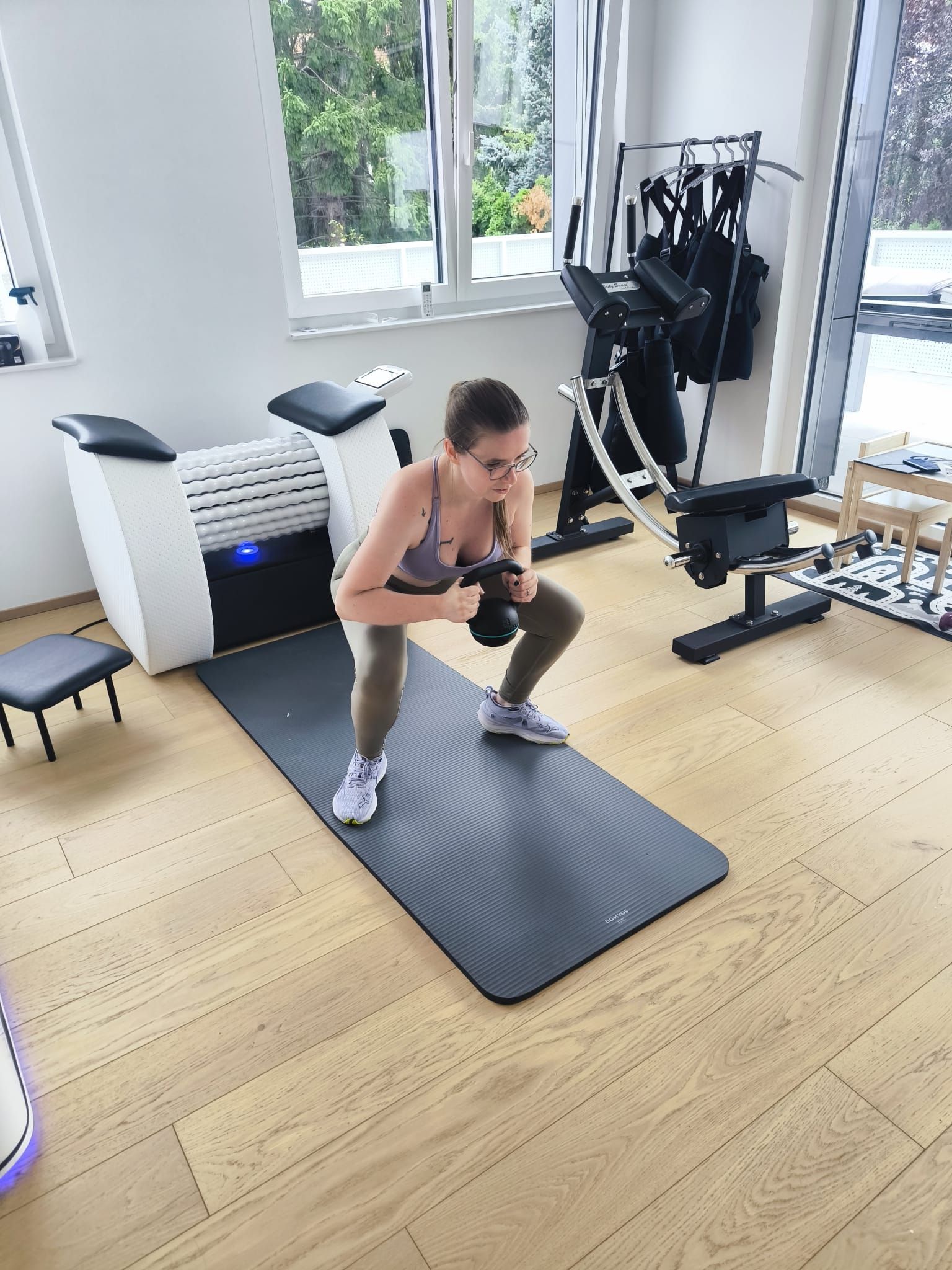 Frau macht Kettlebell-Kniebeugen auf einer grauen Matte in einem Heim-Fitnessstudio. 
