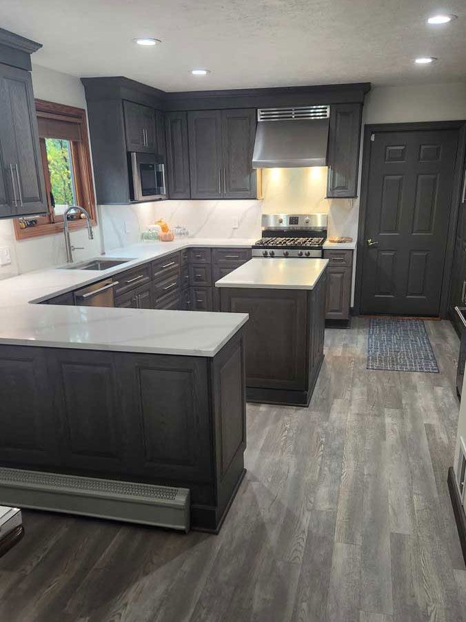 A kitchen with gray cabinets , white counter tops , a stove and a sink.