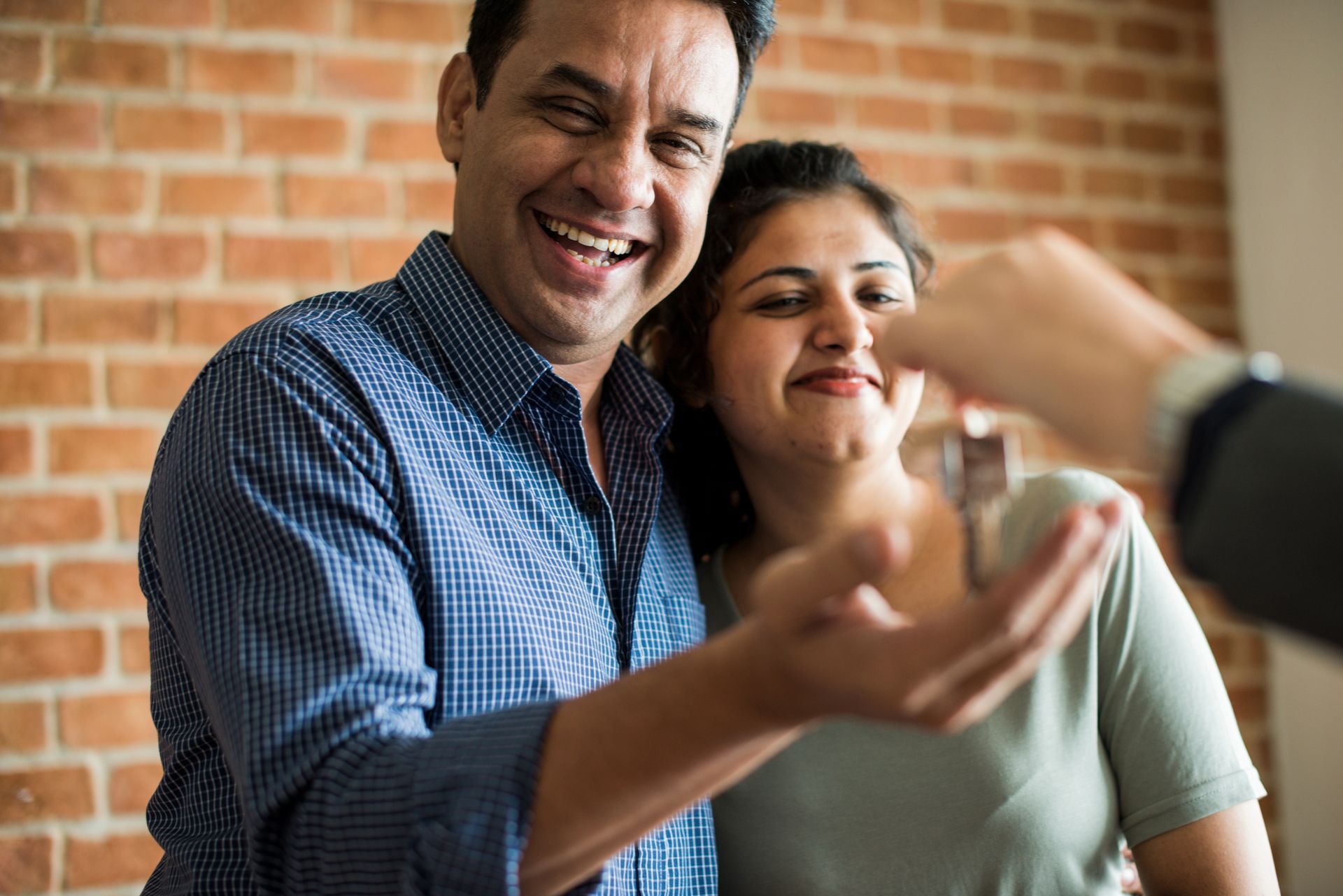 Man and woman smile as they receive keys to a new home from a person in a suit; brick wall in the background.
